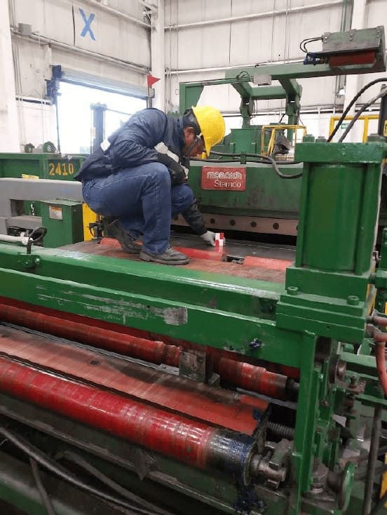 Mantenimiento y limpieza de los rodillos de una máquina aplanadora de metal.