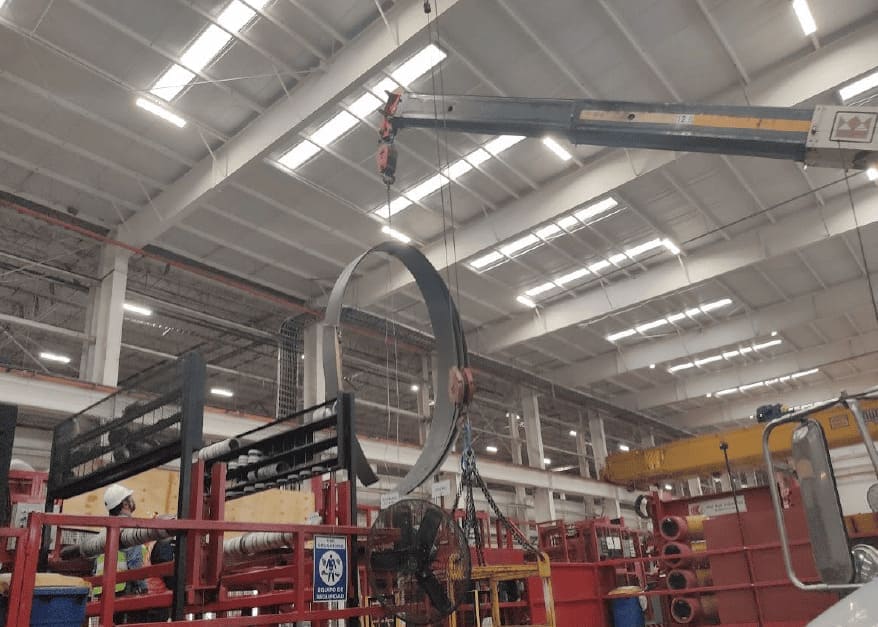 Grúa de puente moviendo un anillo de acero de gran diámetro en planta.