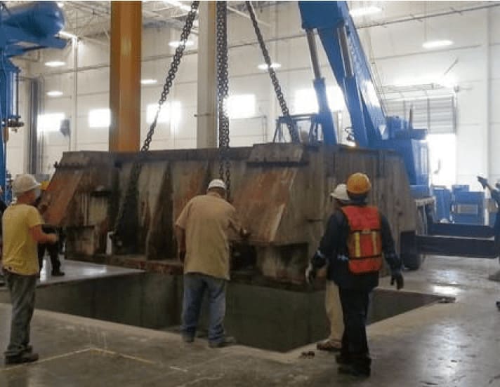 Maniobra de montaje de componente pesado en foso con grúa industrial.